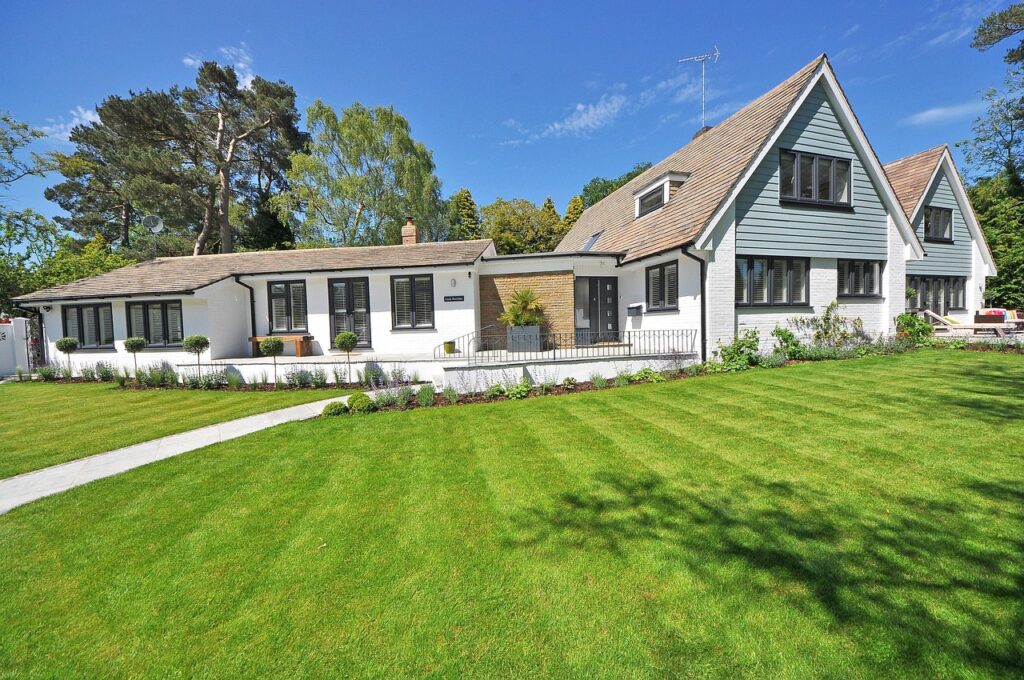 A sunny New England-style luxury home with manicured lawn and garden landscaping.