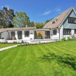 A sunny New England-style luxury home with manicured lawn and garden landscaping.