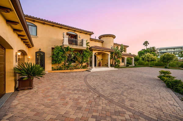 A stucco home with a tile roof, arched entry and a wide paver driveway at dusk.