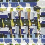 Aerial drone view of a suburban neighborhood showing rooftops, driveways, and a repeating pattern of homes.
